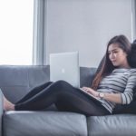 Woman working on laptop and lying on sofa
